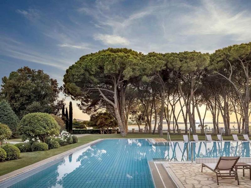 Piscina con acqua limpida circondata da sdraio e pini al tramonto.