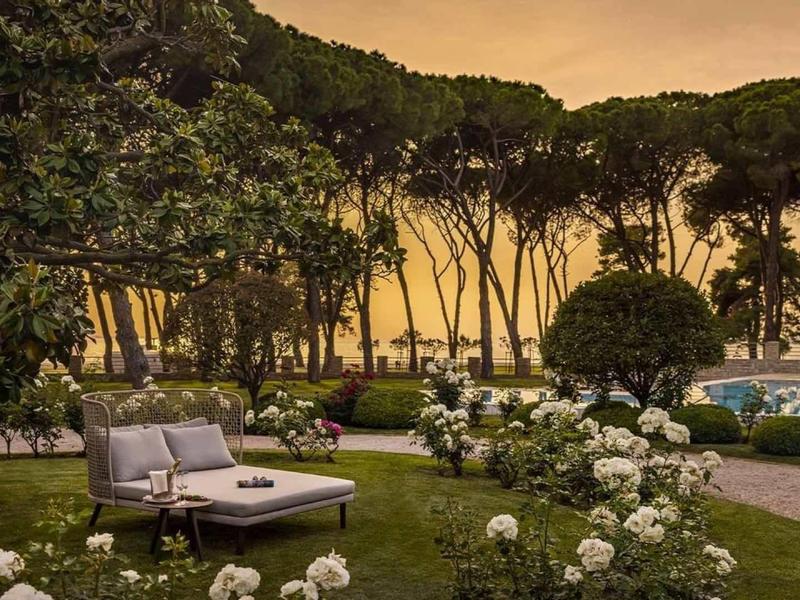 Giardino con zona salotto e fiori bianchi al tramonto, alberi sullo sfondo.