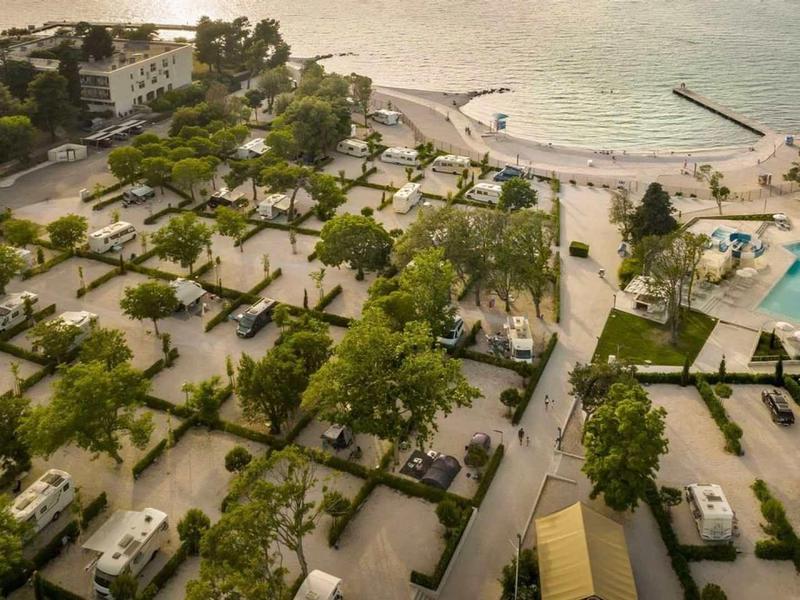 Vista aerea di un resort sulla spiaggia con ville, alberi e una grande piscina accanto al mare.