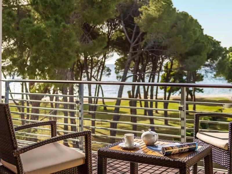 Balcone con sedie e tavolo, vista su alberi e mare sullo sfondo.