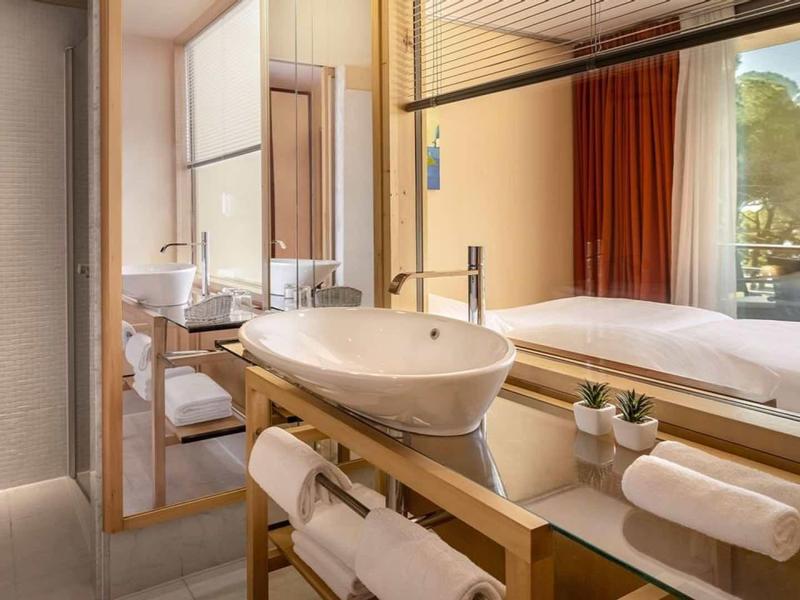 Bagno moderno in hotel con lavabo, grandi specchi e vista sulla camera da letto.