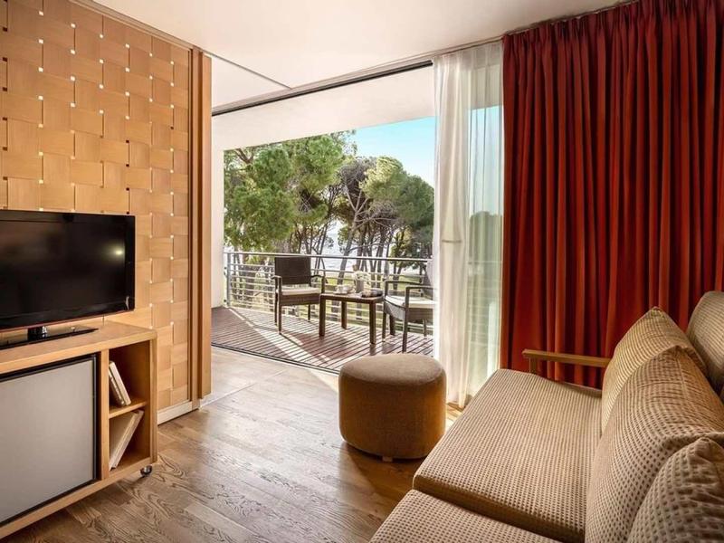 Zona accogliente della camera d'hotel con divano, TV e accesso a una terrazza con tavolo e sedie.