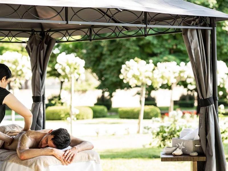 Una donna riceve un massaggio alla schiena all'aperto sotto un gazebo in un giardino.
