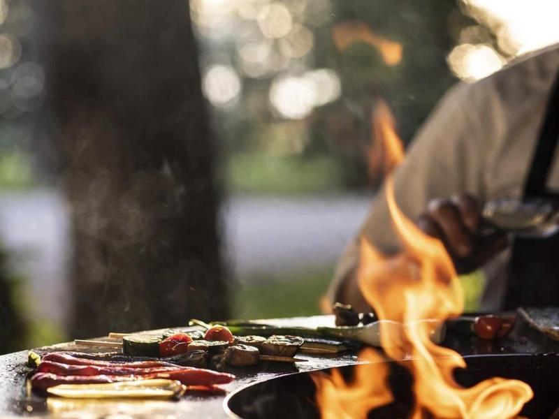 Primo piano di una griglia con verdure e carne, fiamme visibili all'aperto