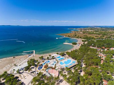 Vue sur la côte avec plage, piscines d'hôtel et zones boisées sous un ciel bleu.