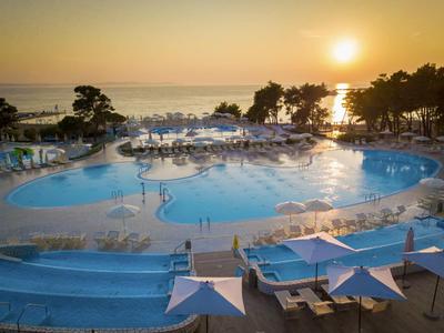 Grand bassin d'hôtel au coucher du soleil avec chaises longues et parasols près de la mer.