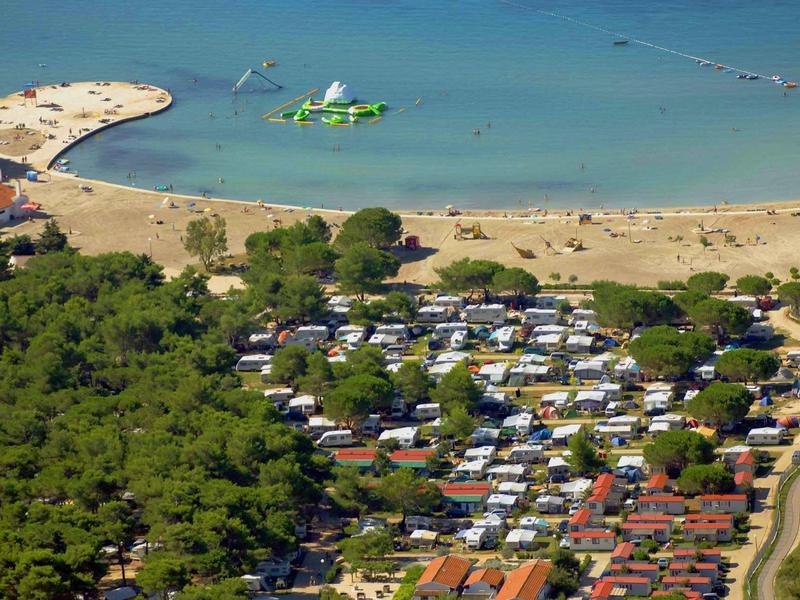 Aerial view of a campsite near a beach with trees and a beach promenade.