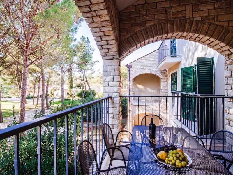 Balcony with metal chairs and table under a stone arch, surrounded by trees.
