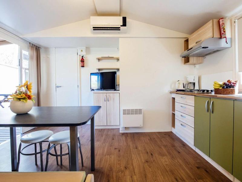 Compact modern kitchen with green lower cabinets, wood flooring, and dining table by the window.