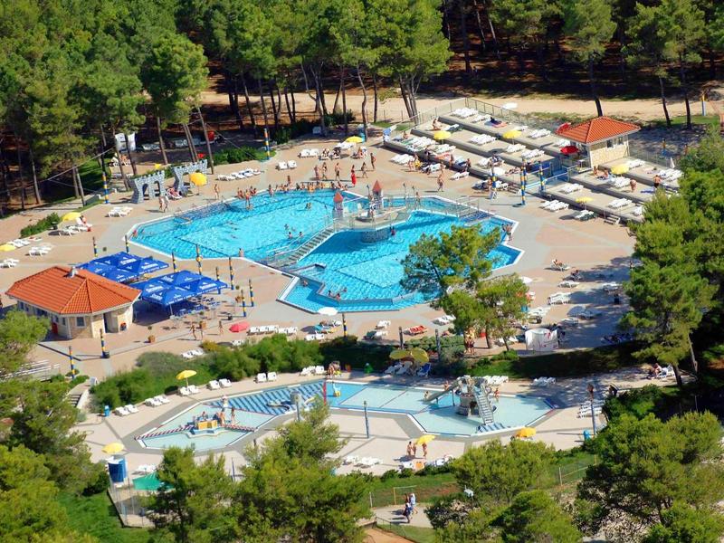 View of a pool area surrounded by trees with lounge chairs and umbrellas.