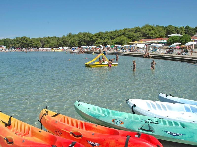Colorful kayaks on the beach with clear water and people along the shore under a blue sky.