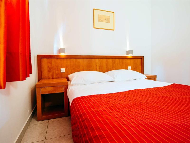 A simple hotel room with a double bed, red curtains, and minimalist furnishings.