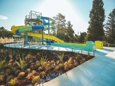 Un parco scivoli d'acqua con scivoli blu e gialli accanto a un giardino curato e alberi.