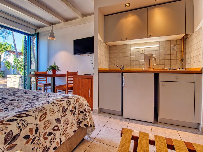 Przytulny pokój hotelowy z aneksem kuchennym, stołem jadalnym i otwartym balkonem w świetle dziennym.