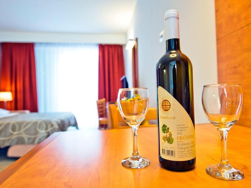 Butelka wina i dwie szklanki na drewnianym stole w pokoju hotelowym z łóżkiem w tle