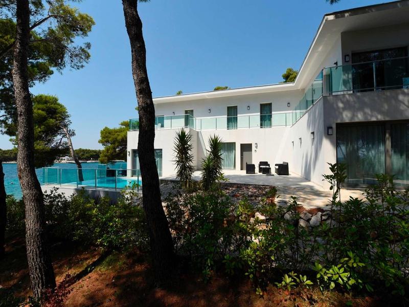 Modernes, zweistöckiges Haus mit großen Glasfenstern, Balkon und umgeben von Bäumen und Sträuchern.