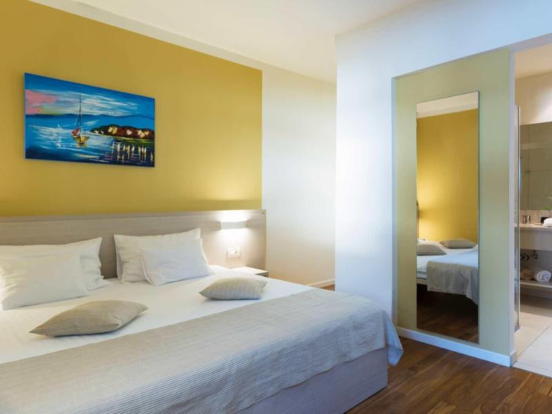 Modernes Schlafzimmer mit großem Bett, weißen Kissen, gelber Wand und Spiegelwand mit Badblick.