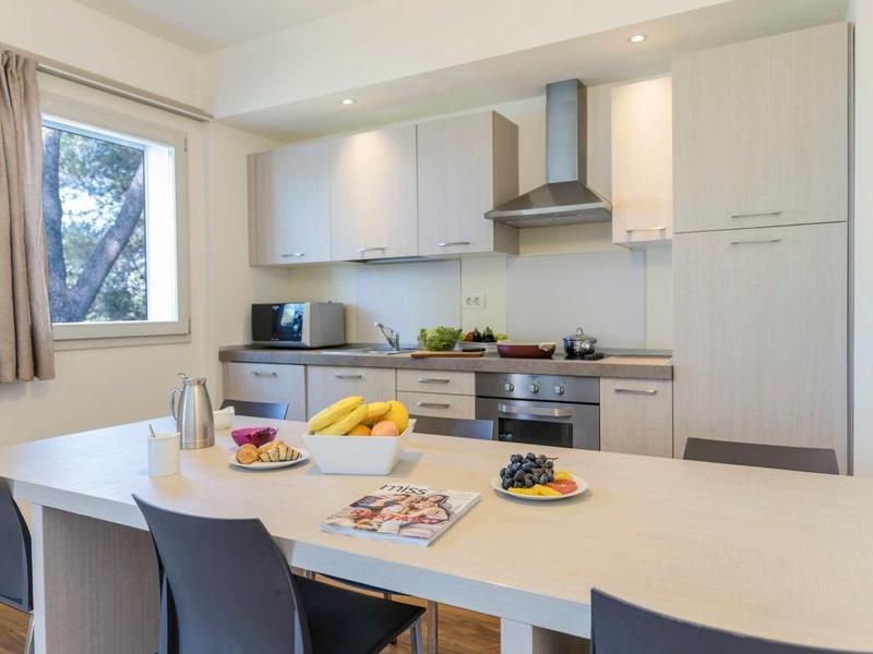 Moderne weiße Küche mit Kochinsel, Barhockern, Obstschalen und Fenster mit Vorhang.