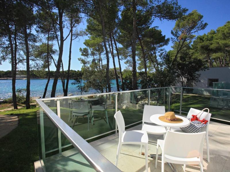 Terrasse mit weißem Möbelset, Blick auf Bäume und blaues Meer im sonnigen Freien.