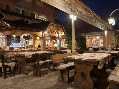 Espace extérieur chaleureux d'un restaurant la nuit avec mobilier en bois rustique et lumière chaude.