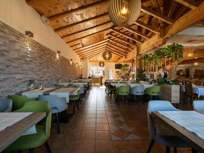 Restaurant chaleureux avec plafond à poutres en bois, chaises vertes et longues tables.
