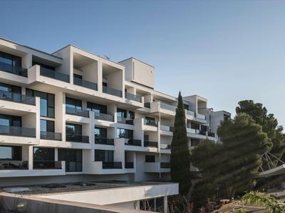 Bâtiment d'hôtel moderne avec plusieurs balcons entouré d'arbres sous un ciel clair.