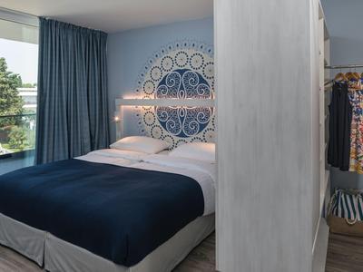 Chambre d'hôtel moderne avec lit double, couvre-lit bleu et balcon donnant sur la verdure.