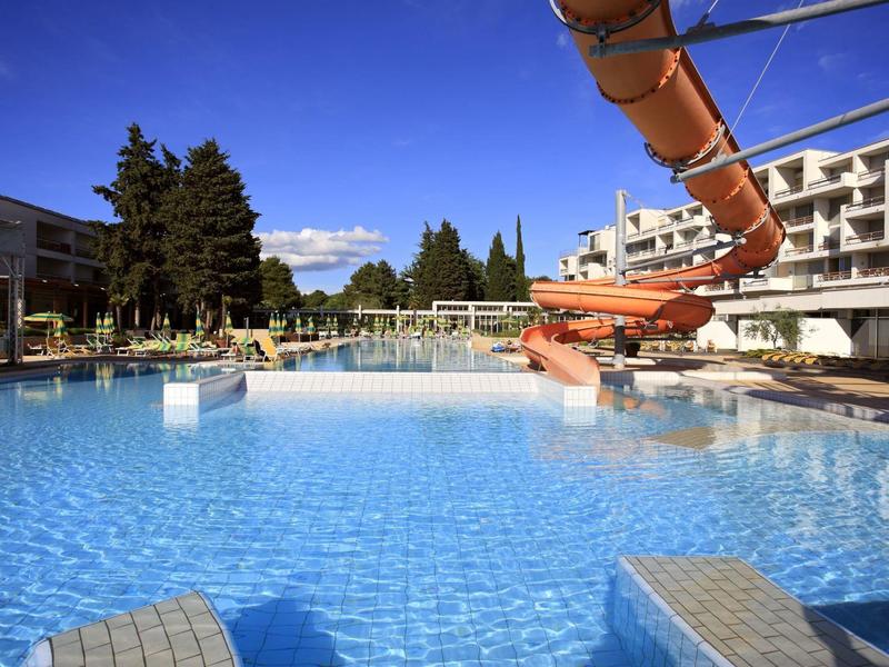Duży basen na zewnątrz z zjeżdżalnią wodną i hotelem pod słonecznym niebem