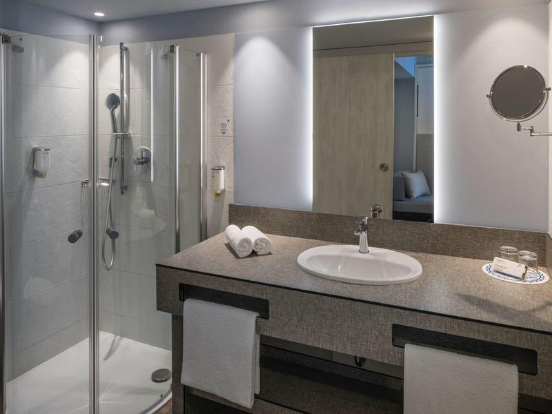 Nowoczesna łazienka hotelowa z szklaną prysznicem, podświetlanym lustrem i umywalką.