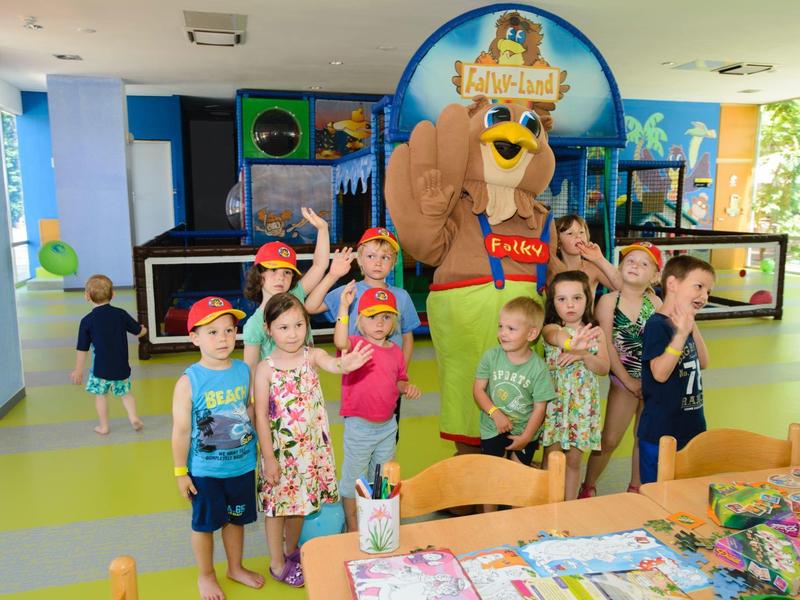 Dzieci radośnie pozują z maskotką ptaka w kolorowej przestrzeni wewnętrznej.