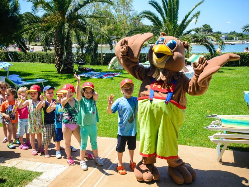 Grupa dzieci stojąca obok dużej maskotki ptaka przy słonecznym basenie