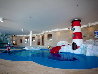 Espace piscine pour enfants avec bassin, toboggan et décor de phare à l'intérieur.