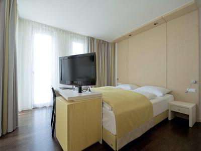 Chambre d'hôtel moderne avec lit double, télévision à écran plat et grandes fenêtres avec rideaux.