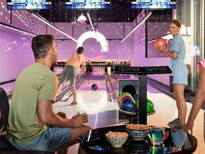 Famille jouant dans une salle de bowling élégante avec éclairage moderne et coin salon confortable.
