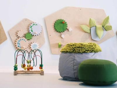 Moderní hotelová hala s barevnými dřevěnými ozubenými koly a pohodlnými zelenými polštáři.