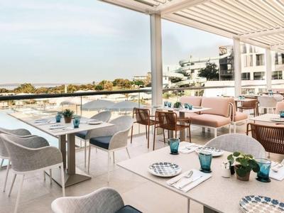 Terrasse de restaurant avec vue sur l'eau et mobilier moderne dans un cadre lumineux.