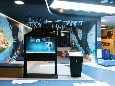 Moderní a barevná hotelová vstupní hala s interaktivním displejem a odpočinkovou zónou.