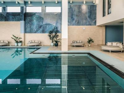 Piscine intérieure moderne avec eau bleue et zones de sièges en arrière-plan.