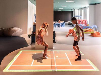 Děti si hrají s interaktivní projekcí na podlaze v moderním vnitřním prostoru.