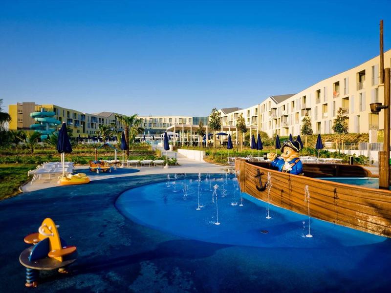 Hotelový areál s hřištěm a vodní plochou za slunečného dne