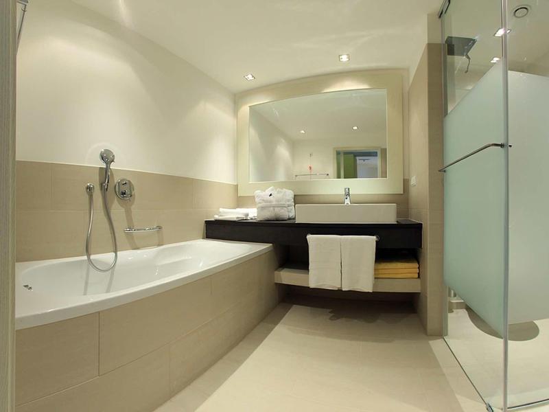 Moderní koupelna s vanou, umyvadlem a samostatným sprchovým koutem v neutrálních barvách.