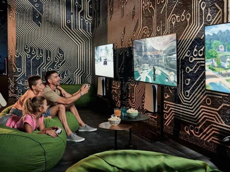 Rodina hrající videohry v moderním, útulném salonu s velkými obrazovkami.