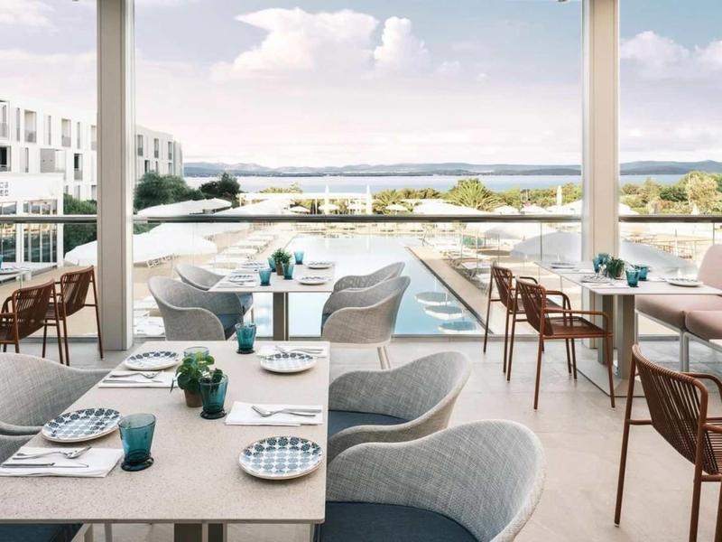 Moderní terasa s jídelními stolky a židlemi s výhledem na bazén a krajinu v pozadí.