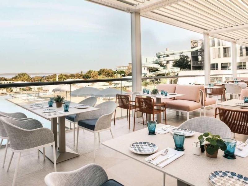 Terasa restaurace s výhledem na vodu a posezením pod pergolou.