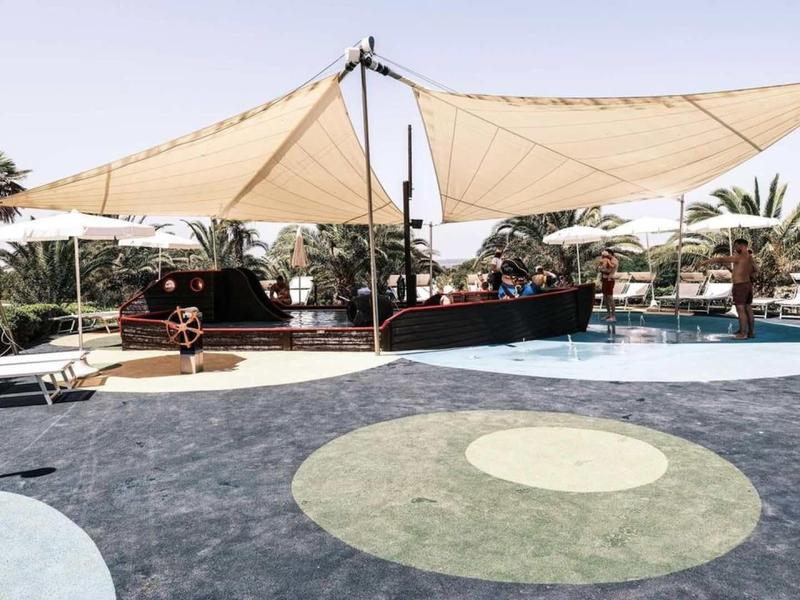 Moderní venkovní prostor s plachtou na stínění, bazénem a lehátky v hotelu.