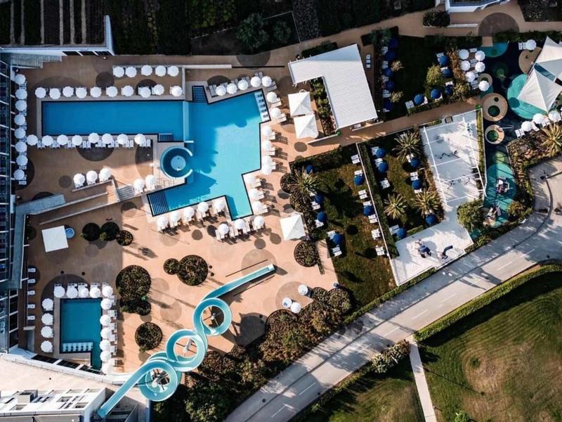 Letecký pohled na hotelovou bazénovou oblast s bazény, lehátky a vodními skluzavkami.