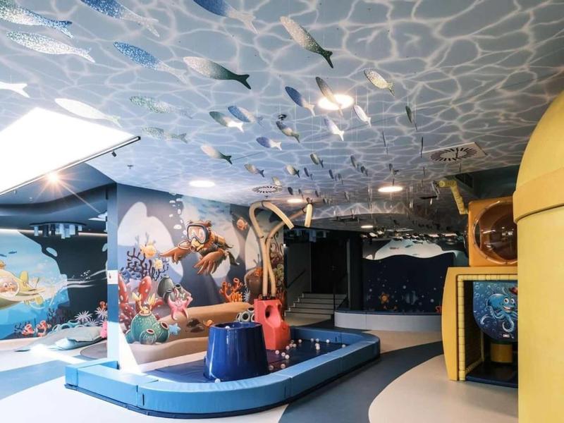 Dětský herní prostor se skluzavkami, lezeckou stěnou a barevným herním vybavením v rekreačním prostoru.