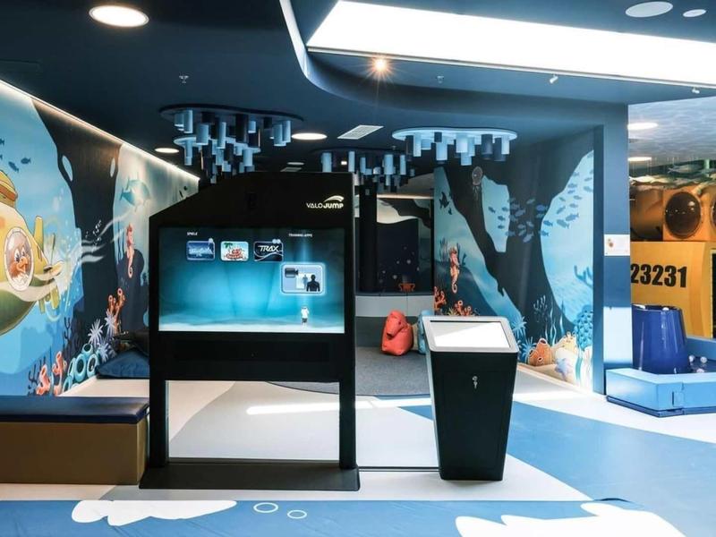 Moderní a barevná hotelová vstupní hala s interaktivním displejem a odpočinkovou zónou.