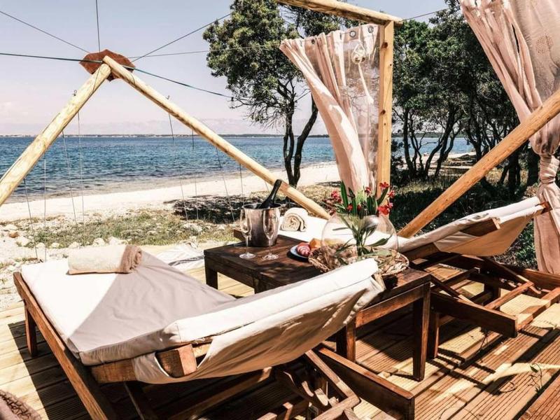 Dřevěná terasa s houpací sítí s výhledem na zalesněnou pláž a moře