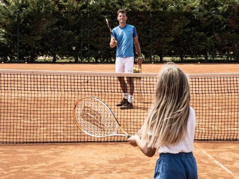 Dva lidé hrají tenis na antukovém kurtu, jedna osoba vrací míček.